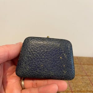 May include: A small, dark blue, leather-covered box with a gold clasp. The box is slightly worn and has a few small scratches.