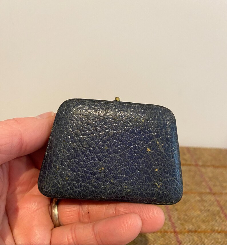 May include: A small, dark blue, leather-covered box with a gold clasp. The box is slightly worn and has a few small scratches.