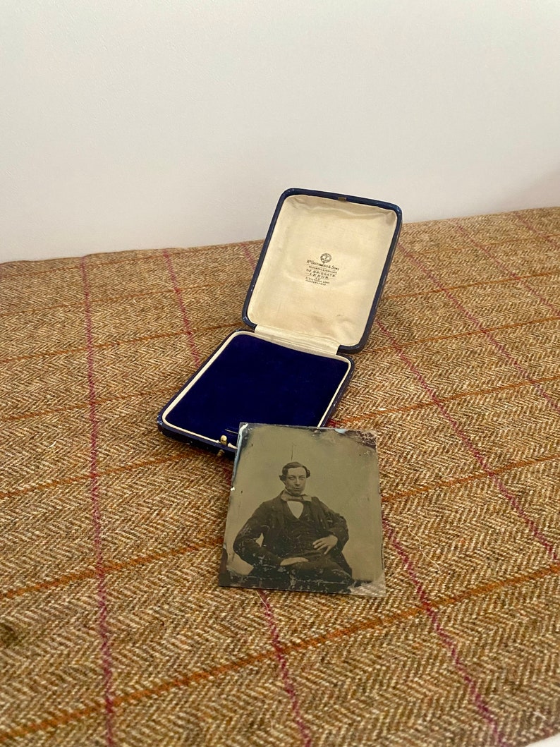 May include: A vintage photograph of a man in a dark suit and bow tie, sitting in a chair. The photo is in a blue velvet lined box with a white label that reads "Greenwood Bros. & Co. Ltd.  Manufacturing Jewellers.  London."