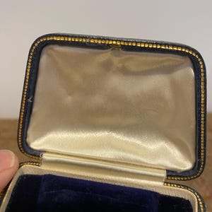 May include: A black velvet-lined jewelry box with a gold trim. The box is open and the inside is lined with white satin.