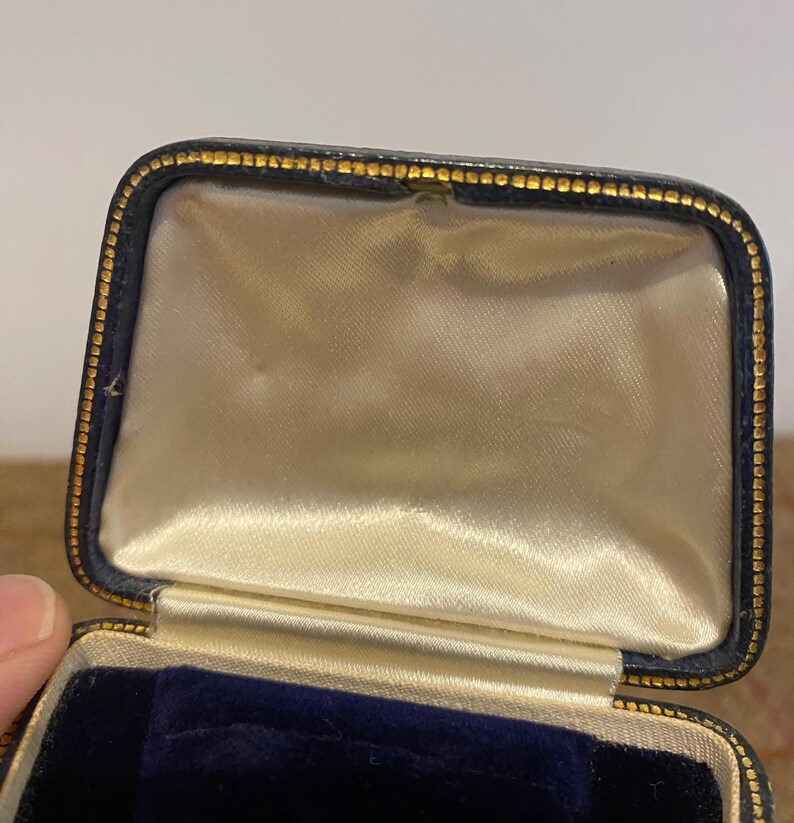 May include: A black velvet-lined jewelry box with a gold trim. The box is open and the inside is lined with white satin.
