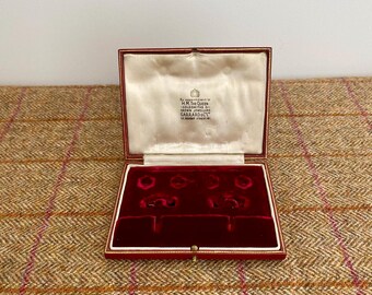 May include: A red velvet lined jewelry box with a red leather exterior. The box has a label that reads "By appointment to H.M. The Queen, Gold and Silversmiths, Garrard & Co. Ltd., 112 Regent Street, W1."