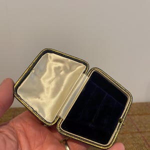 May include: A small, rectangular, black velvet jewelry box with gold trim. The box is open and the interior is lined with white satin.