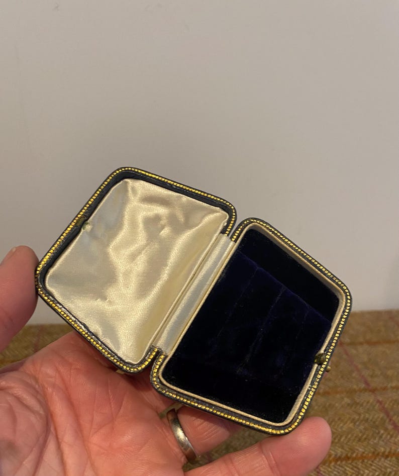 May include: A small, rectangular, black velvet jewelry box with gold trim. The box is open and the interior is lined with white satin.