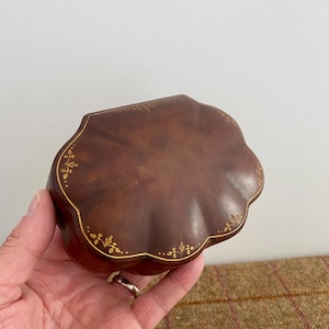 May include: A scalloped, dark brown wooden box with a smooth, polished finish. The lid features a delicate, hand-painted gold floral vine pattern tracing the curved edges, providing a subtle decorative detail on the rich, deep brown surface.