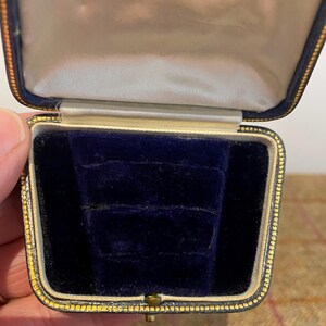 May include: A small, blue velvet ring box with a gold trim. The box is open and empty.