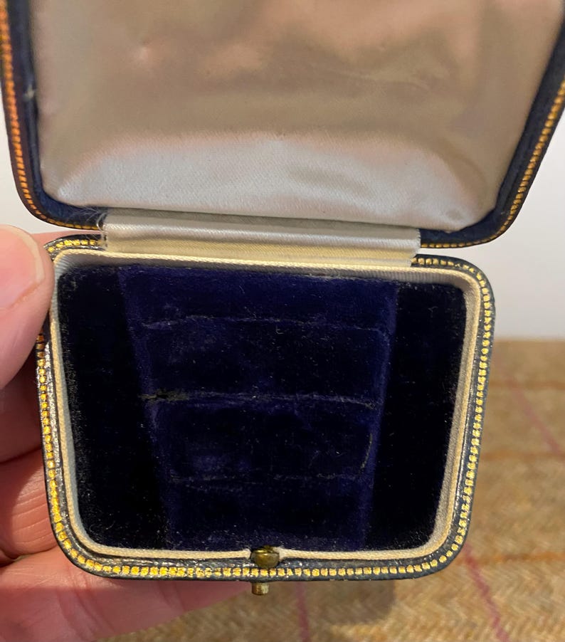 May include: A small, blue velvet ring box with a gold trim. The box is open and empty.