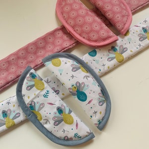 Peut inclure: Deux paires de protège-ceintures de sécurité de voiture en tissu. Une paire est rose avec un motif de soleil blanc et l'autre paire est blanche avec un motif de paon coloré.