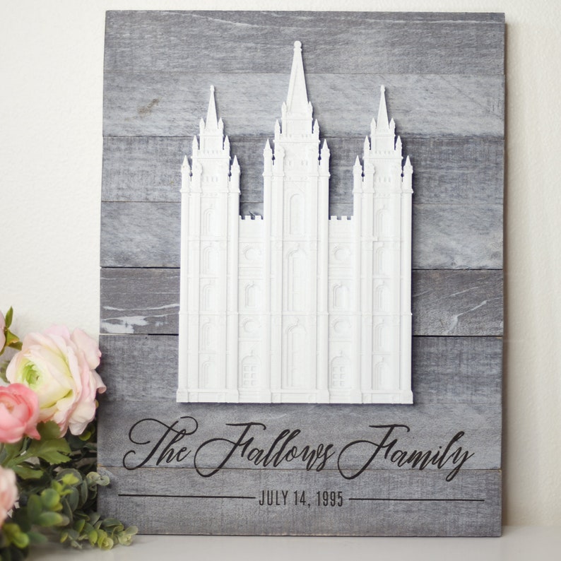 May include: A white wooden sign with a 3D cutout of a temple. The sign is painted gray and has the text "The Fallows Family - JULY 14, 1995" written in black.