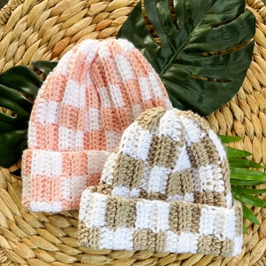 May include: Two crocheted hats with a checkered pattern. One hat is pink and white, the other is brown and white.