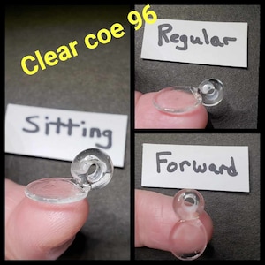 May include: Clear glass COE 96 beads in three positions: sitting, regular, and forward. The beads are clear and have a small loop on the top.