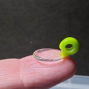 Op de afbeelding: Een kleine, heldere, ronde glazen lens met een felgroene plastic lus aan de zijkant.