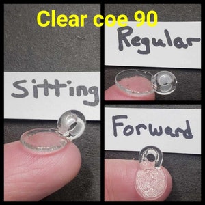 May include: Clear coe 90 Regular glass bead in three positions: sitting, forward, and regular. The bead is clear and has a small hole in the center.