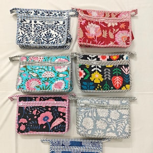 May include: A collection of seven quilted pouches with various floral and geometric patterns. The pouches feature a rectangular shape with a small loop and a striped border. Colors include blue, red, black, teal, and white.