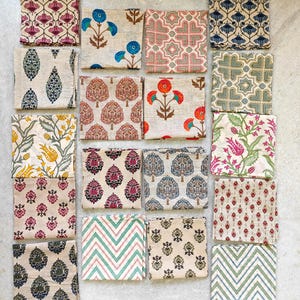 May include: A collection of folded square fabric napkins with various floral and geometric patterns. The napkins feature designs in shades of blue, red, pink, green, and yellow on a neutral background. The patterns include stylized flowers, trees, and geometric shapes.
