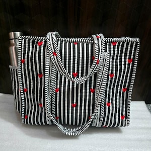 May include: Black and white striped tote bag with red heart accents. The bag has a water bottle pocket and matching striped handles. The tote is rectangular and appears to be made of quilted fabric.