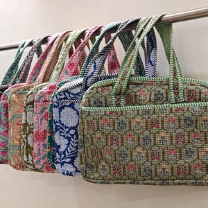 Può includere: Una fila di borse tote colorate con motivi floreali. Le borse sono in vari colori, tra cui verde, rosa e blu, e hanno manici coordinati. Le borse sono appese a una barra di metallo.