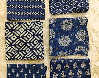 Puede incluir: Un juego de seis servilletas de tela cuadradas en varios tonos de azul marino y crema. Cada servilleta presenta un patrón de estampado en bloque distinto, incluyendo diamantes geométricos, motivos florales estilizados y hojas.