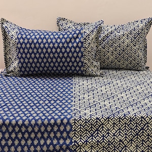 以下が含まれることがあります： 青と白の幾何学模様のベッドセット。セットには枕カバー2枚とフィットシーツが含まれています。枕カバーとシーツには、ダイヤモンドと花の形の繰り返し模様があります。配色は濃い青とオフホワイトです。