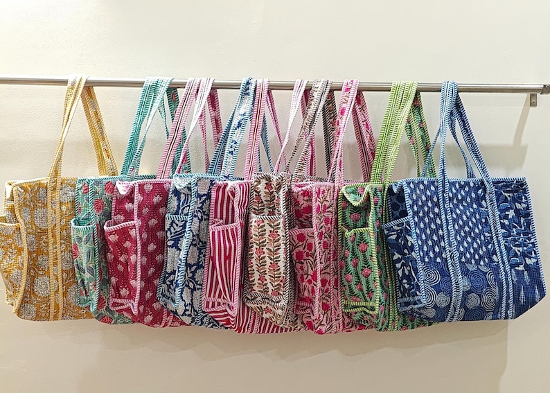 May include: A collection of colorful tote bags with various floral and geometric patterns. The bags are made of fabric and have matching straps and exterior pockets. The color palette includes yellow, teal, red, blue, and green.
