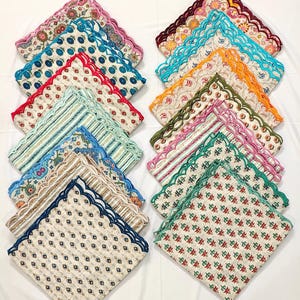 Puede incluir: Una colección de servilletas de tela estampadas y coloridas. Cada servilleta cuadrada presenta un diseño único con bordes festoneados en varios colores, como rosa, azul, rojo y verde. Los patrones incluyen diseños florales, geométricos y a rayas.