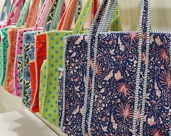 May include: A row of quilted tote bags hanging on a metal rod. Each bag features distinct patterns including floral prints, polka dots, and geometric designs in various colors like navy blue, lime green, orange, pink, and teal with striped handles.
