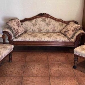 May include: A set of three antique wooden chairs with floral patterned upholstery. The chairs include a loveseat and two armchairs.