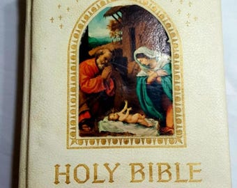 May include: A white leather-bound Holy Bible with a gold-embossed title and a depiction of the nativity scene on the front cover.