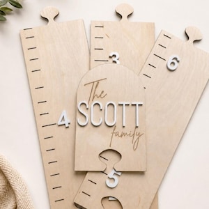 May include: Wooden growth chart puzzle pieces with the text "The SCOTT family" and numbers 3, 4, 5, and 6. The pieces are light brown with black measurement markings and white numbers. The puzzle pieces are designed to measure a child's height.