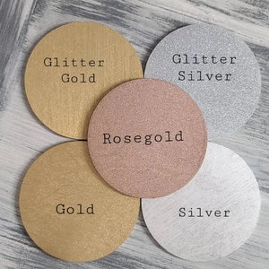 May include: Four round coasters with different finishes: glitter gold, rose gold, gold, and glitter silver. The coasters are arranged in a circle on a wooden surface.