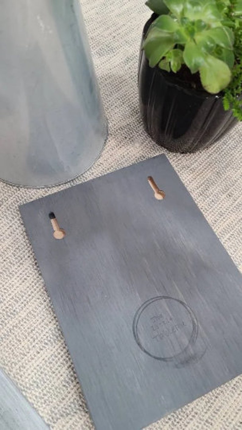 May include: A gray wooden sign with two holes for hanging. The sign has a distressed finish and the text "The Little  Treasury" is printed in a circle in the lower right corner.
