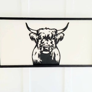 May include: Black and white silhouette of a Highland cow's head with a fluffy mane, framed in a black wood frame.