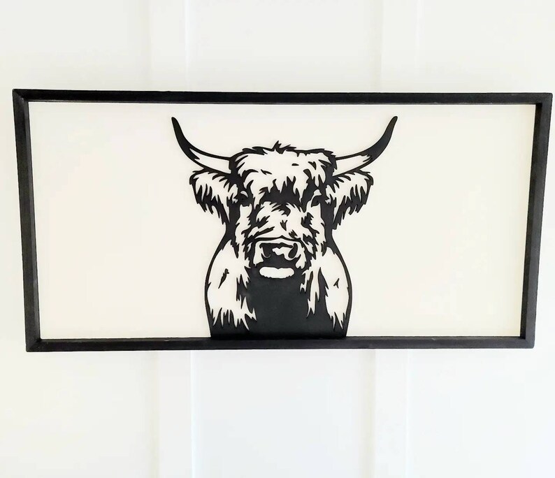 May include: Black and white silhouette of a Highland cow's head with a fluffy mane, framed in a black wood frame.