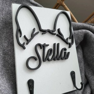May include: White wooden key holder with a black silhouette of a French Bulldog's head and the name "Stella" in a cursive font. The key holder has two black metal hooks.