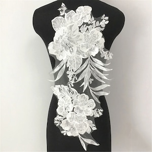 May include: White floral lace applique with delicate flowers and leaves. This lace applique is perfect for adding a touch of elegance to any project.