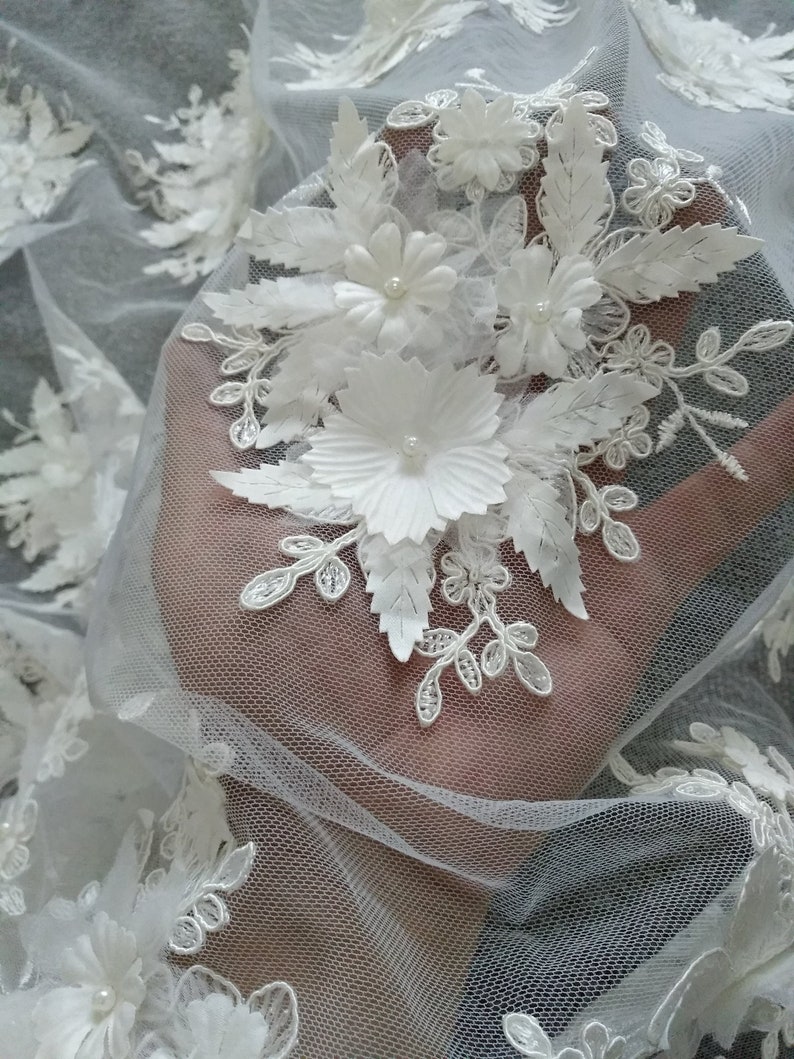May include: White floral lace fabric with 3D flowers and leaves. The fabric is sheer and delicate, with a fine mesh pattern.