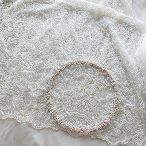 May include: White beaded fabric with a delicate, intricate pattern. The fabric is sheer and has a subtle shimmer.