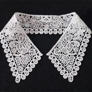 May include: White lace collar with a delicate floral pattern. The collar is made of a soft, lightweight fabric and has a scalloped edge.