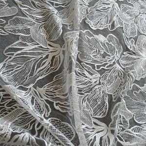 May include: White floral lace fabric with a delicate, intricate pattern. The lace is sheer and has a soft, flowing texture.