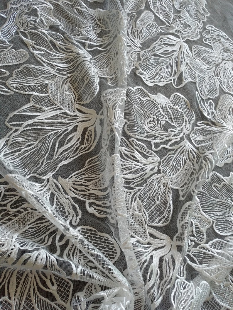 May include: White floral lace fabric with a delicate, intricate pattern. The lace is sheer and has a soft, flowing texture.