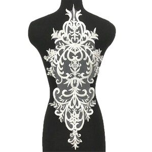 May include: White lace applique featuring a floral and scroll design. The applique is shaped like a teardrop and is ideal for adding a touch of elegance to any garment.