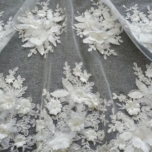 May include: White floral lace fabric with 3D flowers and leaves. The lace is delicate and intricate, with a soft, flowing texture. The fabric is perfect for adding a touch of elegance to any project.