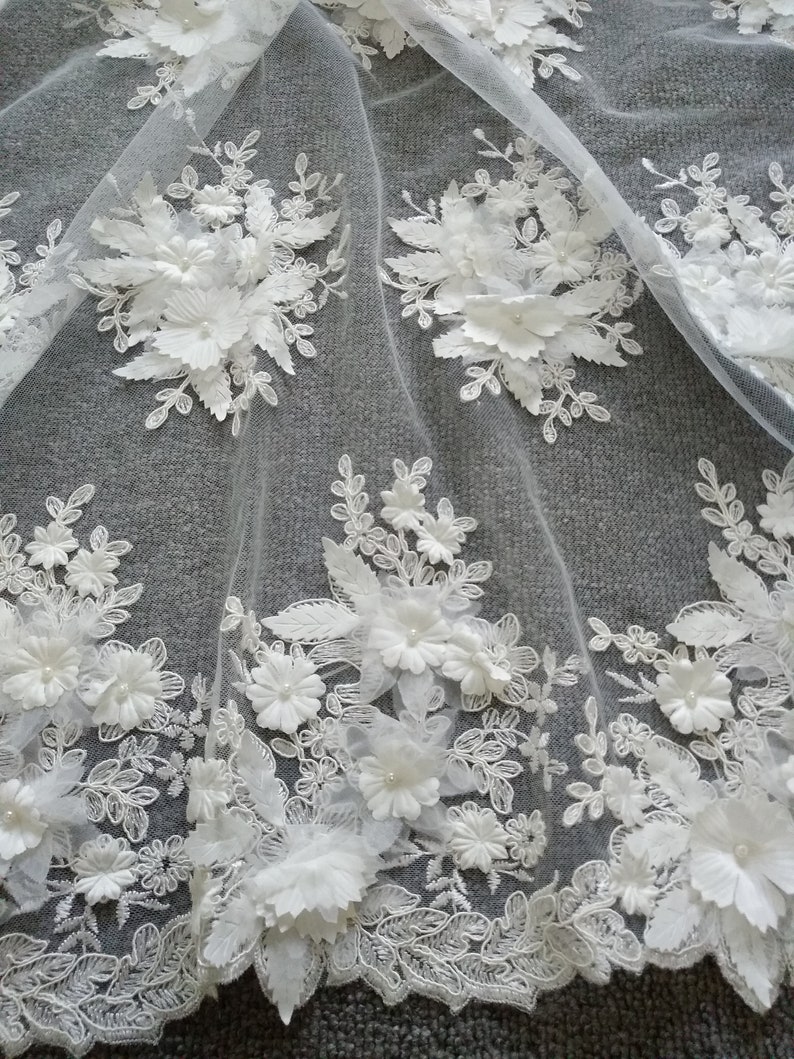 May include: White floral lace fabric with 3D flowers and leaves. The lace is delicate and intricate, with a soft, flowing texture. The fabric is perfect for adding a touch of elegance to any project.