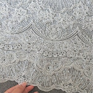 May include: White beaded lace fabric with a delicate floral pattern. The fabric is sheer and has a soft, flowing texture.