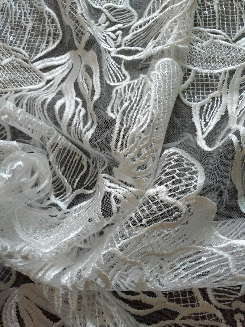 May include: White lace fabric with a floral pattern. The lace is delicate and intricate, with a soft, flowing texture.