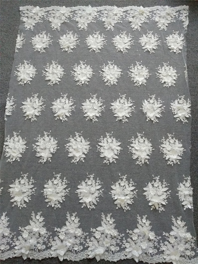 May include: White floral lace fabric with a repeating pattern of 3D flowers. The fabric is delicate and has a soft, feminine look.