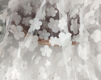 May include: White tulle fabric with white 3D flower embellishments. The fabric has a subtle sparkle.