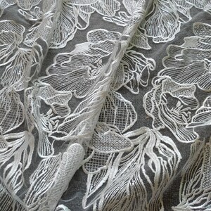 May include: White floral lace fabric with a delicate pattern. The lace is sheer and has a soft, flowing texture.