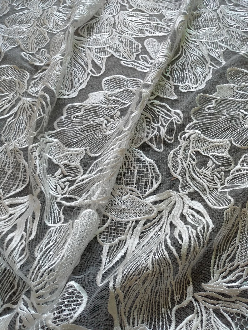 May include: White floral lace fabric with a delicate pattern. The lace is sheer and has a soft, flowing texture.