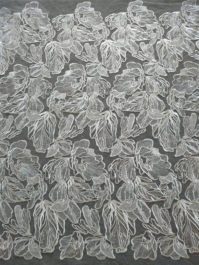 May include: White floral lace fabric with a delicate, intricate design. The lace features a repeating pattern of stylized flowers with a textured, raised effect.